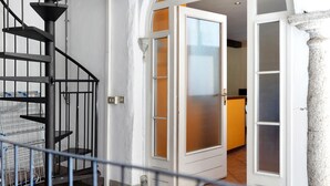 Un escalier avec une rampe en métal, une porte blanche dotée de panneaux en verre dépoli et une colonne en pierre.