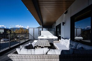 A balcony with a hot tub, wicker furniture, and a view of mountains. - Base Camp Revelstoke 2023 (Revelstoke)
