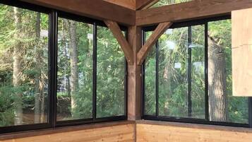 A wooden cabin with a large window, a ceiling fan, and a seating area with cushions.