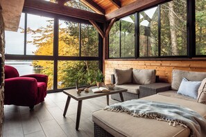 Une pièce chaleureuse avec une grande fenêtre, un canapé, un fauteuil rouge et une table en bois.