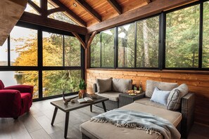 A cozy room with a wooden ceiling, large windows, a sofa, a red chair, and a table with a bowl and books. - Camp David Beautiful five bedrooms  Private beach (Kearney)