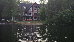Un edificio a due piani con facciata rossa e ampie finestre, affacciato su un lago con alberi sullo sfondo.