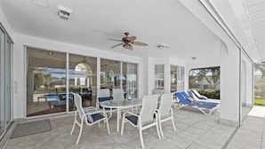 A covered patio with a glass door leading to a pool area, outdoor seating, and a ceiling fan. - Bella Vista Villa - Waterfront Retreat with Gulf Access & Private Pool (Cape Coral)
