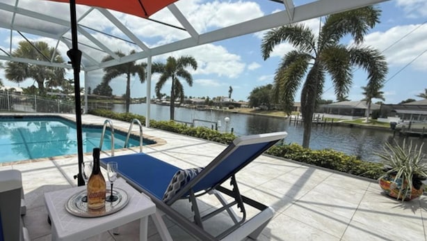 A poolside lounge area with a view of a lake, palm trees, and a covered patio. - Bella Vista Villa - Waterfront Retreat with Gulf Access & Private Pool (Cape Coral)