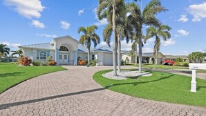 A residential property with a paved driveway, palm trees, and a well-maintained lawn. - Bella Vista Villa - Waterfront Retreat with Gulf Access & Private Pool (Cape Coral)