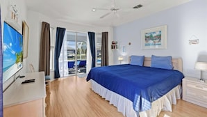 A bedroom with a large bed, a ceiling fan, a TV, and a view of the outdoors. - Bella Vista Villa - Waterfront Retreat with Gulf Access & Private Pool (Cape Coral)