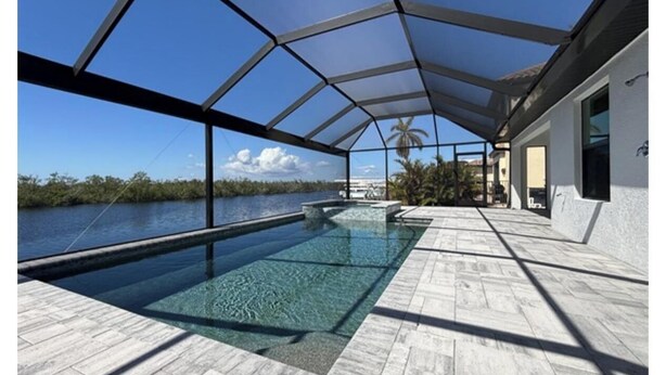 An infinity pool with a clear view of the water and palm trees, surrounded by a covered patio area. - Great fall rates! Canal views! Book now! (Cape Coral)