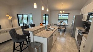A modern kitchen with a central island, stainless steel appliances, and a dining area with a table and chairs. - Great fall rates! Canal views! Book now! (Cape Coral)