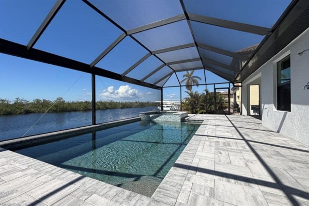 An infinity pool with a clear view of the water and palm trees, surrounded by a covered patio area.