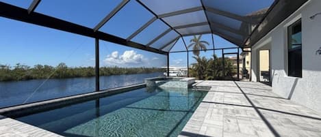 An infinity pool with a clear view of the water and palm trees, surrounded by a covered patio area.