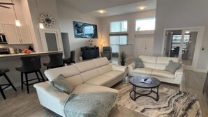 A modern living room with a sectional sofa, a coffee table, and a dining area with chairs. - Great fall rates! Canal views! Book now! (Cape Coral)