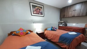 A hotel room with two beds, each with a blue blanket and a white towel. There is a wooden cabinet and a framed picture on the wall. - We are located in the Historic Center of Cusco, behind the Cathedral, Plaza Mayor. (Cusco)