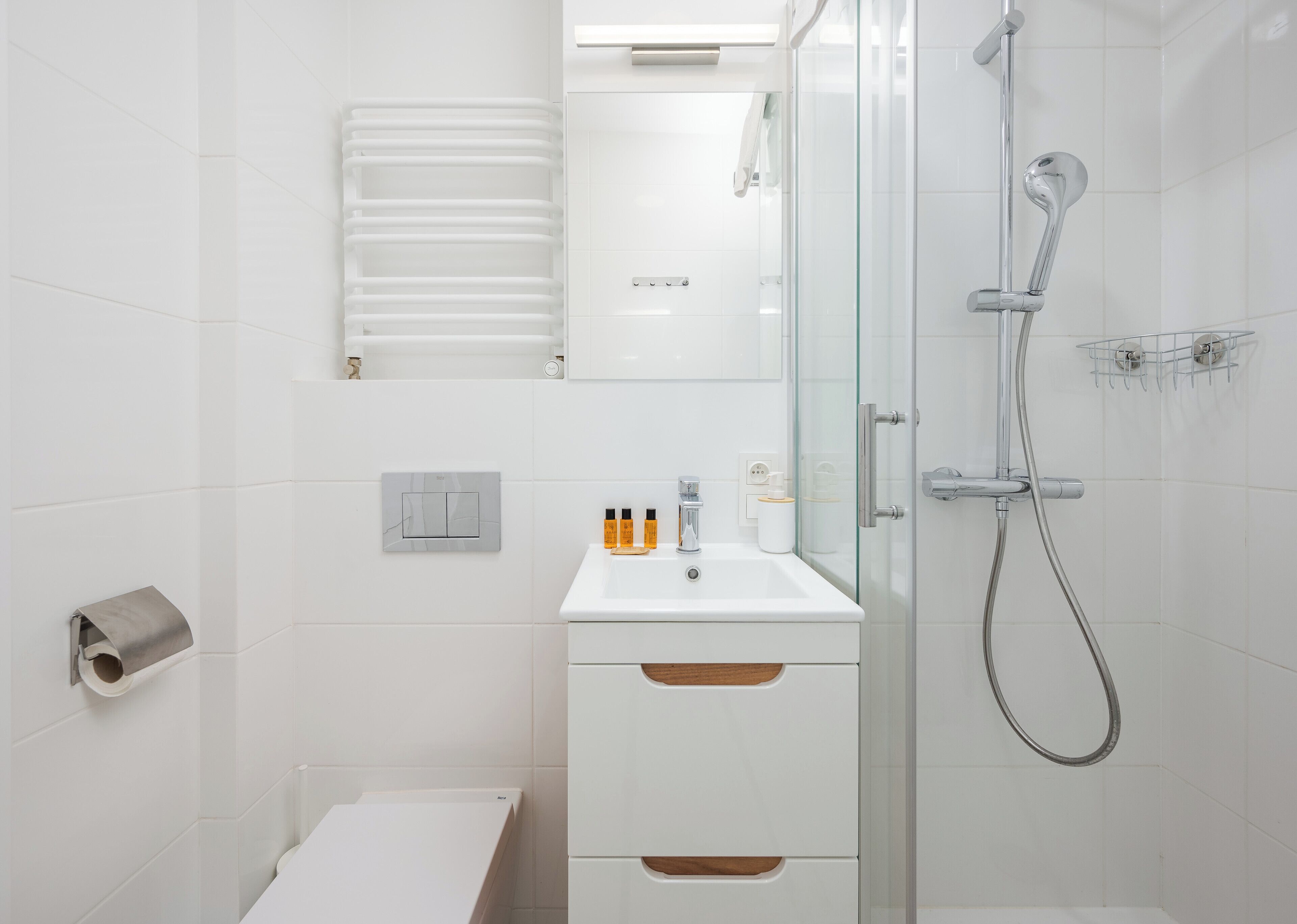 Une salle de bain moderne avec une douche à parois de verre, un lavabo blanc avec un miroir et des toilettes dotées d’un porte-serviettes en papier.