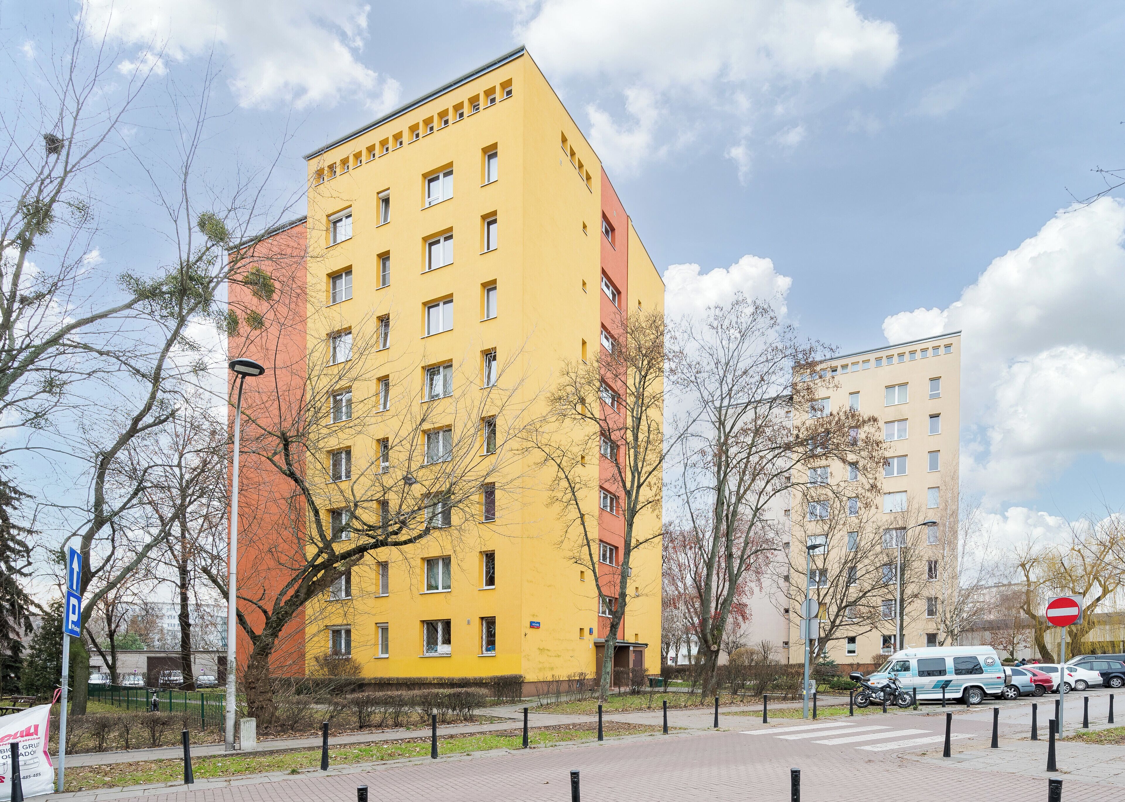 Un bâtiment jaune doté de nombreuses fenêtres et de balcons, entouré d’arbres et de voitures garées.