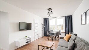 Una sala de estar moderna con un televisor de pantalla plana, un sofá, una mesa de centro y un comedor con sillas y una mesa.
