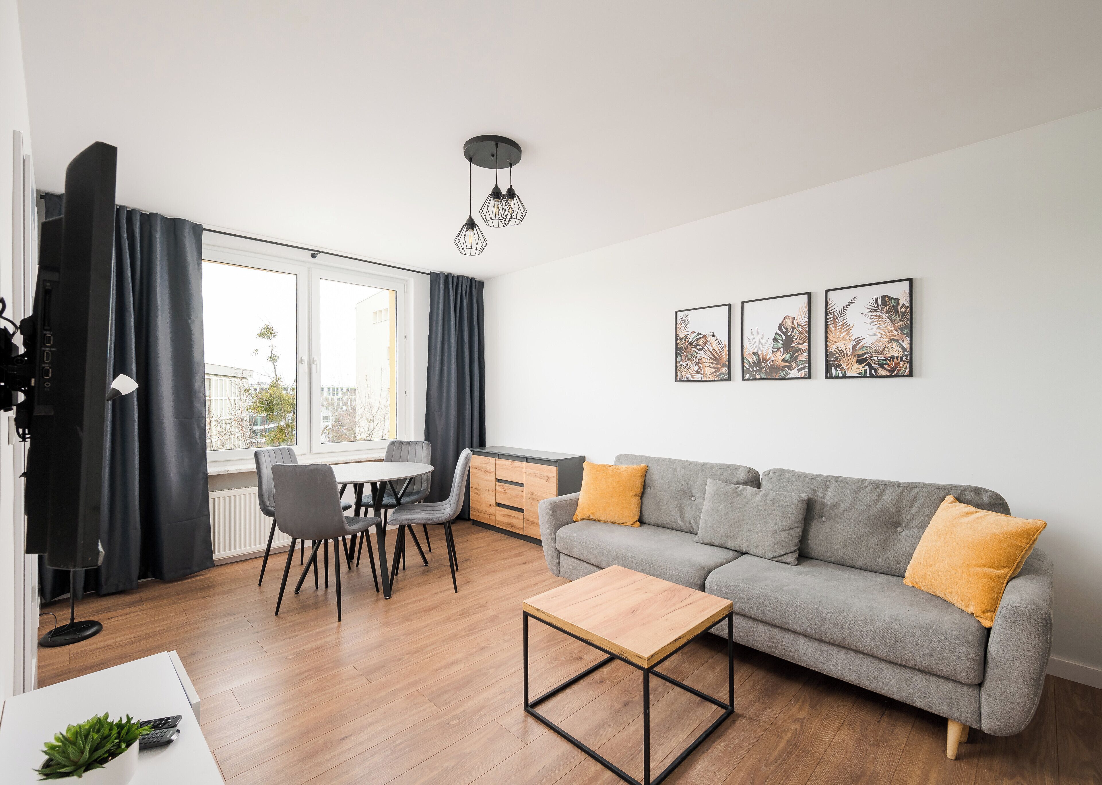 A modern living room with a grey sofa, wooden coffee table, and a dining area with chairs and a table.