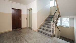 Un pasillo con una puerta de madera, un ascensor de vidrio y una escalera con barandillas de metal.