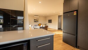 A modern kitchen with a large island, dark cabinetry, and a built-in dishwasher. - Serenity Hideaway House A (Twizel)