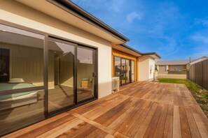 A modern house with a wooden deck, large sliding glass doors, and a visible bedroom with a bed and a chair. - Serenity Hideaway House A (Twizel)
