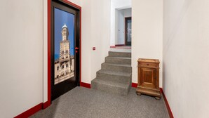 Un pasillo con un cuadro enmarcado de un edificio, escaleras con alfombra y un pequeño armario de madera.