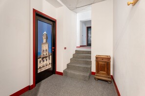 Un pasillo con un cuadro enmarcado de un edificio, escaleras con alfombra y un pequeño armario de madera.
