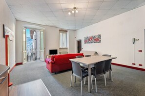 A modern room with a dining table, chairs, a red sofa, a TV, and a painting on the wall.
