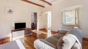 Amplia sala de estar con piso de madera, un sofá, televisor y techo con vigas a la vista.