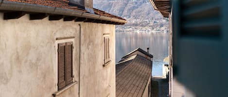 Una calle estrecha con edificios, vista a un lago y montañas al fondo.