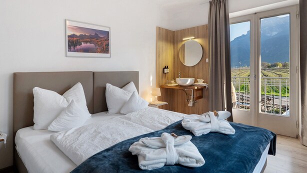 Habitación de hotel con cama, baño con lavamanos, espejo y vista panorámica por la ventana.