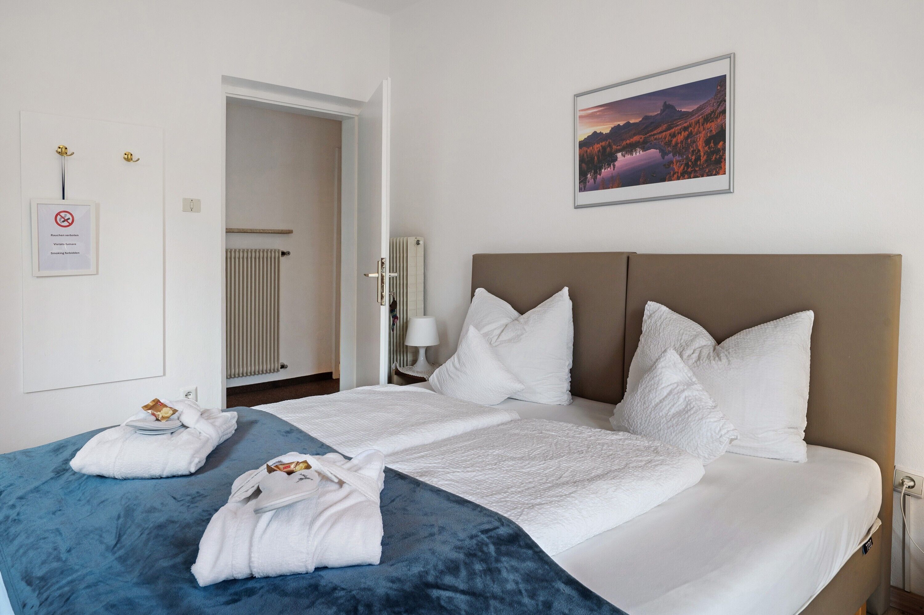 Ein Hotelzimmer mit einem Bett, zwei Handtüchern, einem gerahmten Bild, einem Heizkörper und einer Tür.