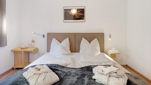 Ein Hotelzimmer mit Bett, Kissen, einem Nachttisch mit Lampe, einem Wandbild und einer kleinen Ablage mit Handtuch und Glas.