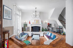 Een ruime woonkamer met een open haard, zithoek en een trap.