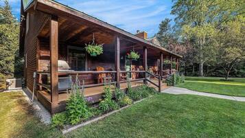 Una cabaña de madera con un porche, mobiliario exterior y una zona de barbacoa.