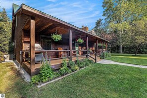 A wooden cabin with a porch, outdoor seating, and a grill area. - Majestic Maple Escapes | Hot Tub | Firepit | Deck | Large Yard (Lake Ann)