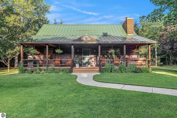 A rustic cabin with a covered porch, a chimney, and a well-maintained lawn.