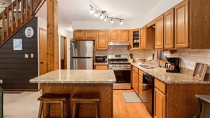 Una cocina con armarios de madera, encimeras de granito, electrodomésticos de acero inoxidable y una escalera de madera.
