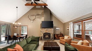 Una sala de estar acogedora con chimenea de piedra, sofás verdes y marrones, un comedor con mesa y sillas, y ventanas amplias que ofrecen una vista.