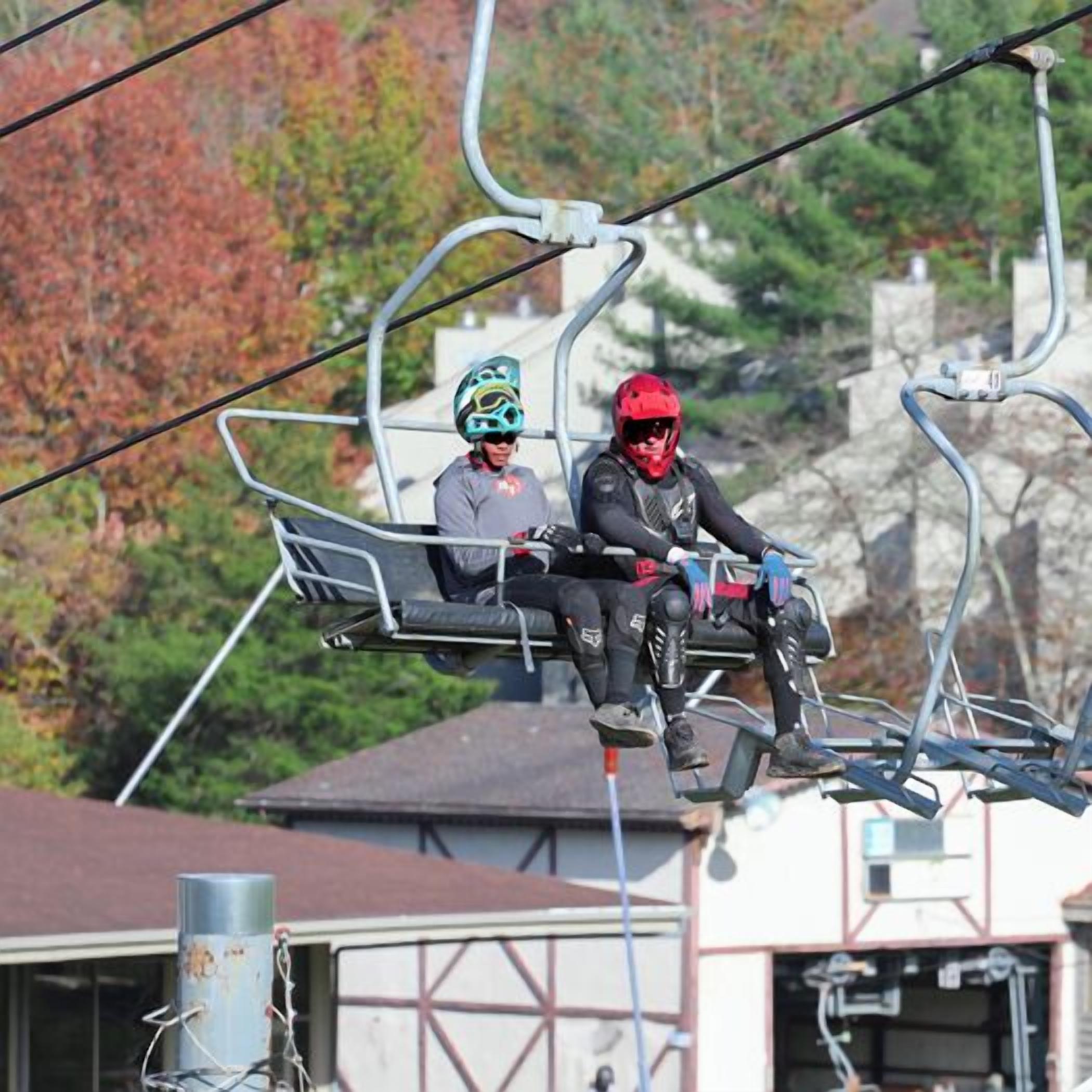 Deux personnes dans un télésiège, avec une chaîne de montagnes en arrière-plan.