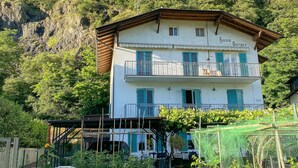 A two-story building with a balcony, surrounded by lush greenery and a mountainous backdrop. - Room 'Haus Burger Vilpian  4' with Mountain View and Wi-Fi (Vilpiano)