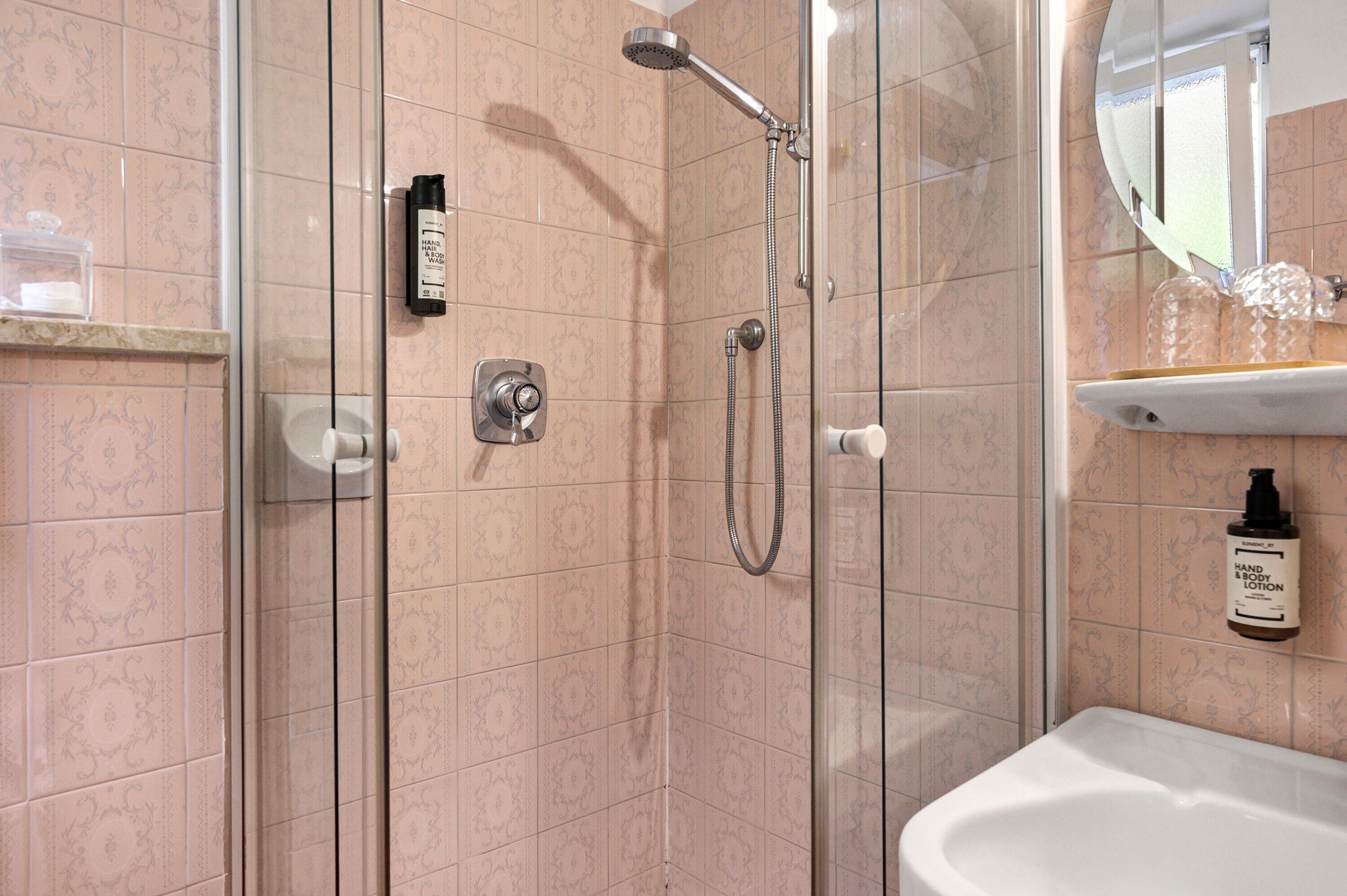 A shower with a handheld showerhead, a wall-mounted control, and a hand soap dispenser.