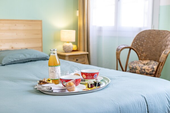 Una bandeja de desayuno bien preparada sobre una cama con cabecera de madera, una botella de jugo de naranja y diversos alimentos para el desayuno.