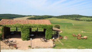 Un espacio de estar al aire libre cubierto con mesas y sillas, rodeado de un exuberante paisaje verde y colinas al fondo.