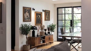 Una sala moderna con una mesa de comedor de vidrio, un mueble de madera con plantas y obras de arte colgadas en la pared.