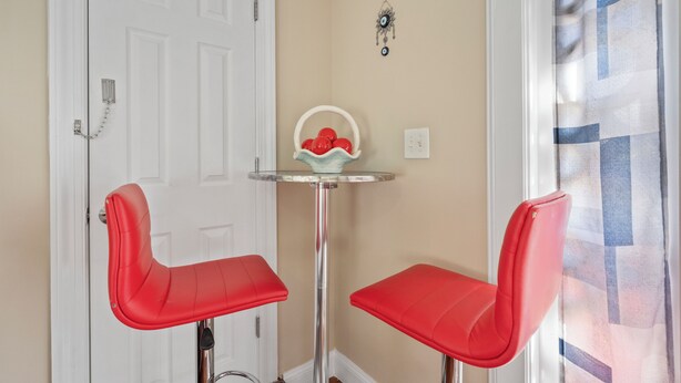 A room with two red chairs, a white door, a small table with a red fruit bowl, and a wall-mounted decoration. - National Harbor Suite 2 (Fort Washington)