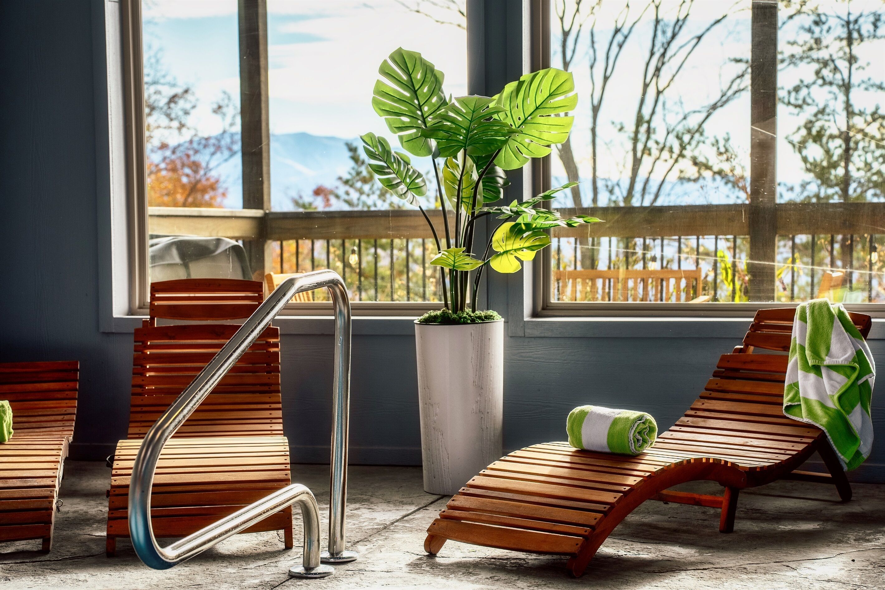 A sunlit room with wooden lounge chairs, a metal handrail, and a potted plant.