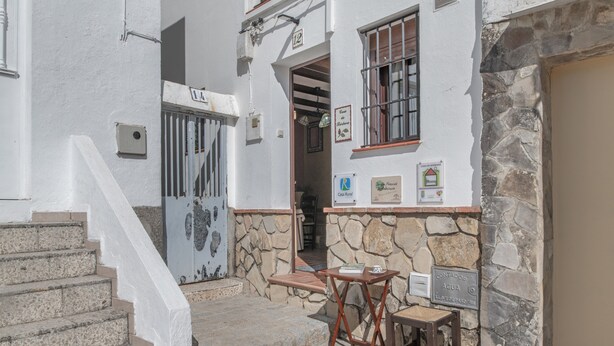 A white building with stone walls, a wooden bench, a small table, and a staircase leading to a door marked '12'. - Holiday Home 'De Bárbara' with Balcony and Air Conditioning (Alcalá de los Gazules)