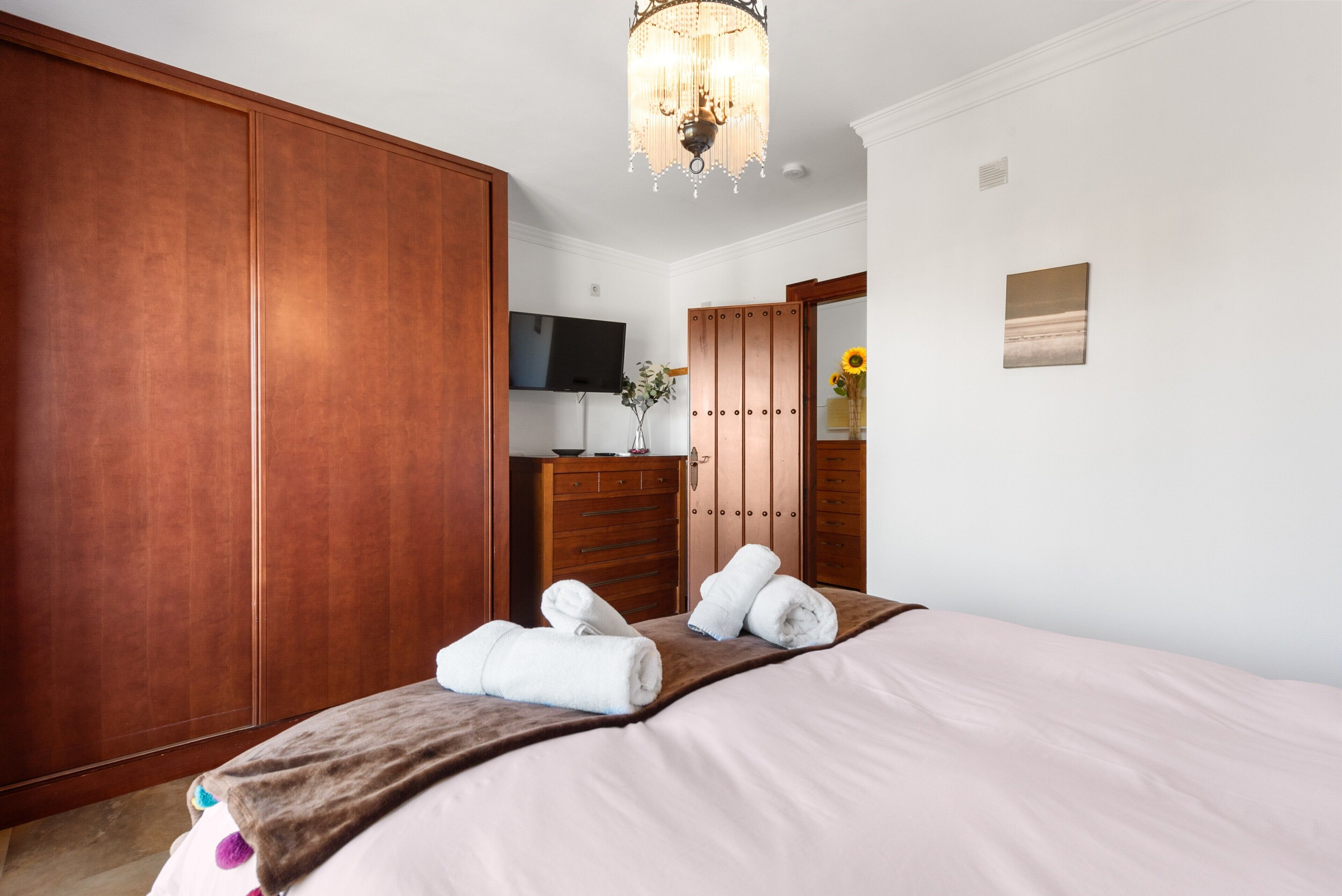 A hotel room with a large wardrobe, a television, a mirror, and a bed with towels.
