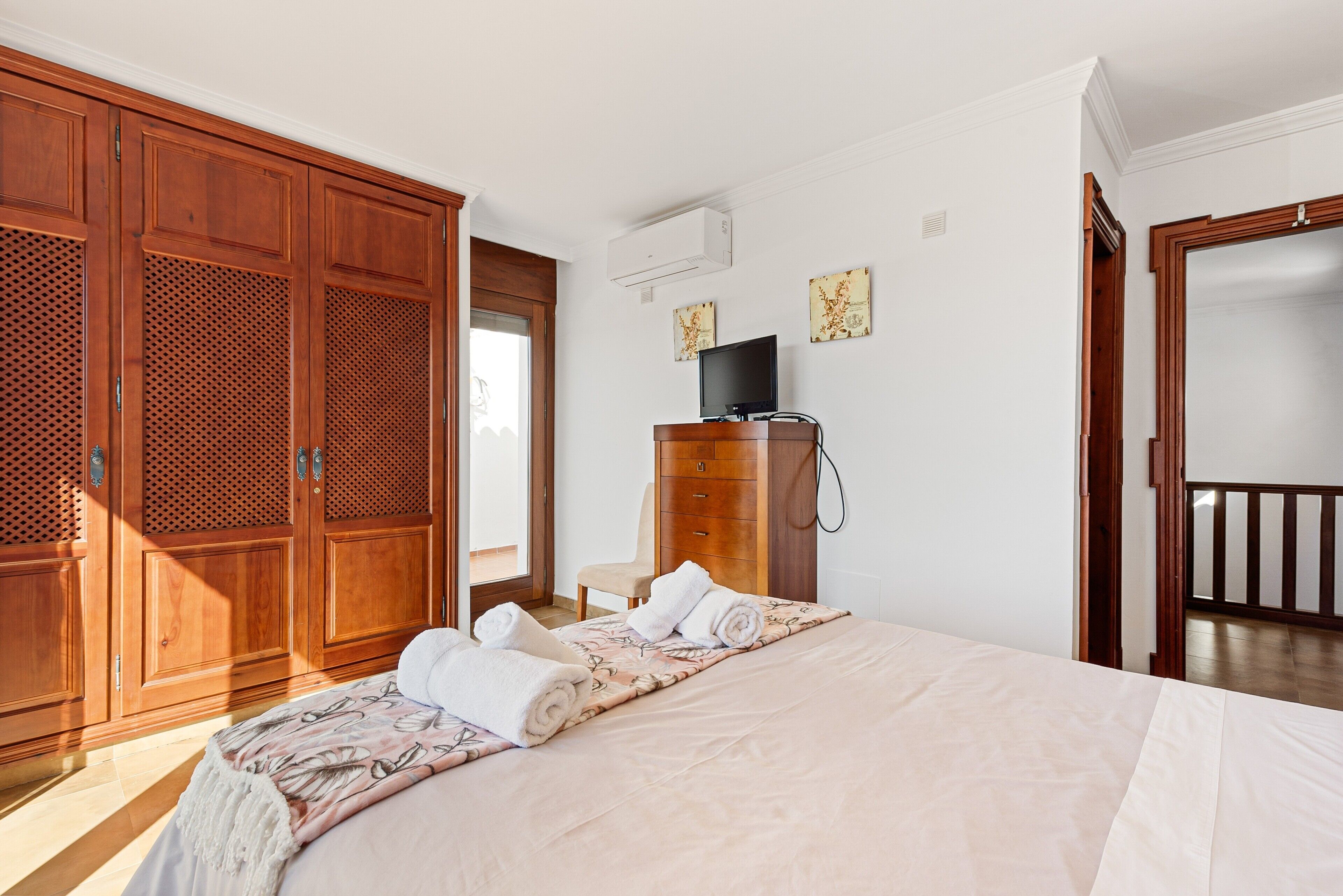 Un dormitorio con cama, armario de madera, televisor y una obra de arte en la pared.
