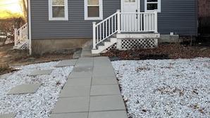 A two-story residential building with a gray exterior, white trim, and a front porch with a white railing.