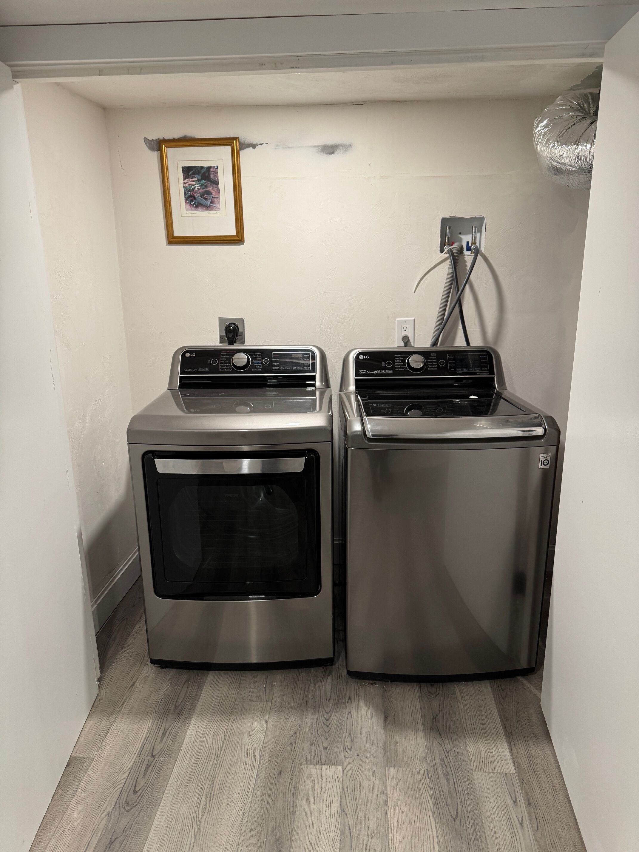 A laundry room with two stainless steel front-loading washers and dryers, a small framed picture on the wall, and a visible electrical outlet.